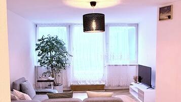 A modern living room with a sectional sofa, a potted plant, and a television on a white stand.