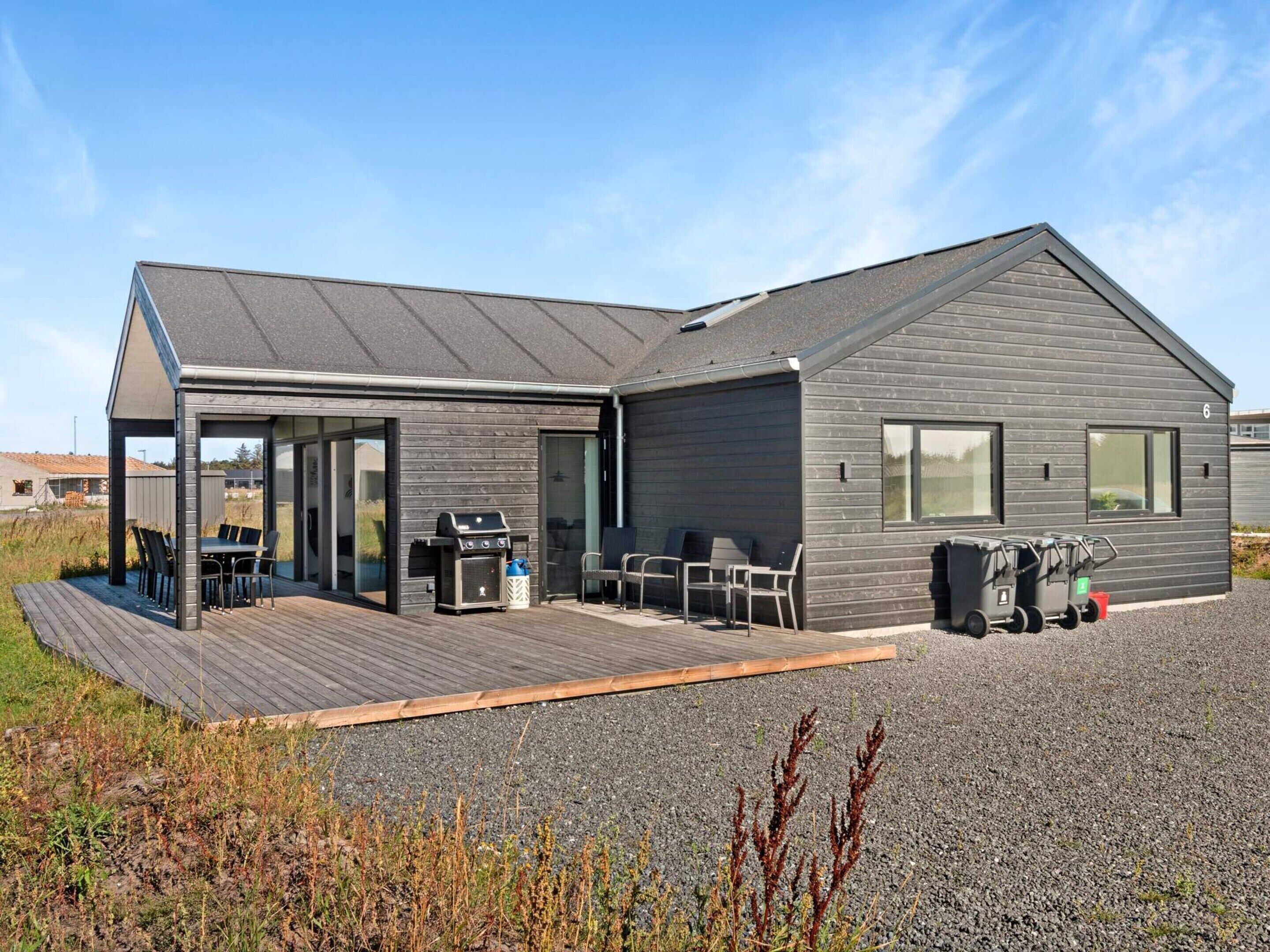 A modern house with a covered patio, a barbecue, and a gravel driveway.