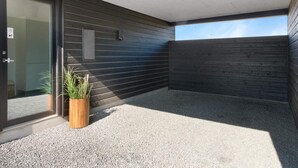 A modern building exterior with a dark wooden facade, a gravel ground, and a wooden planter with grass. - 5 Star Holiday Home in Lokken (Lokken)