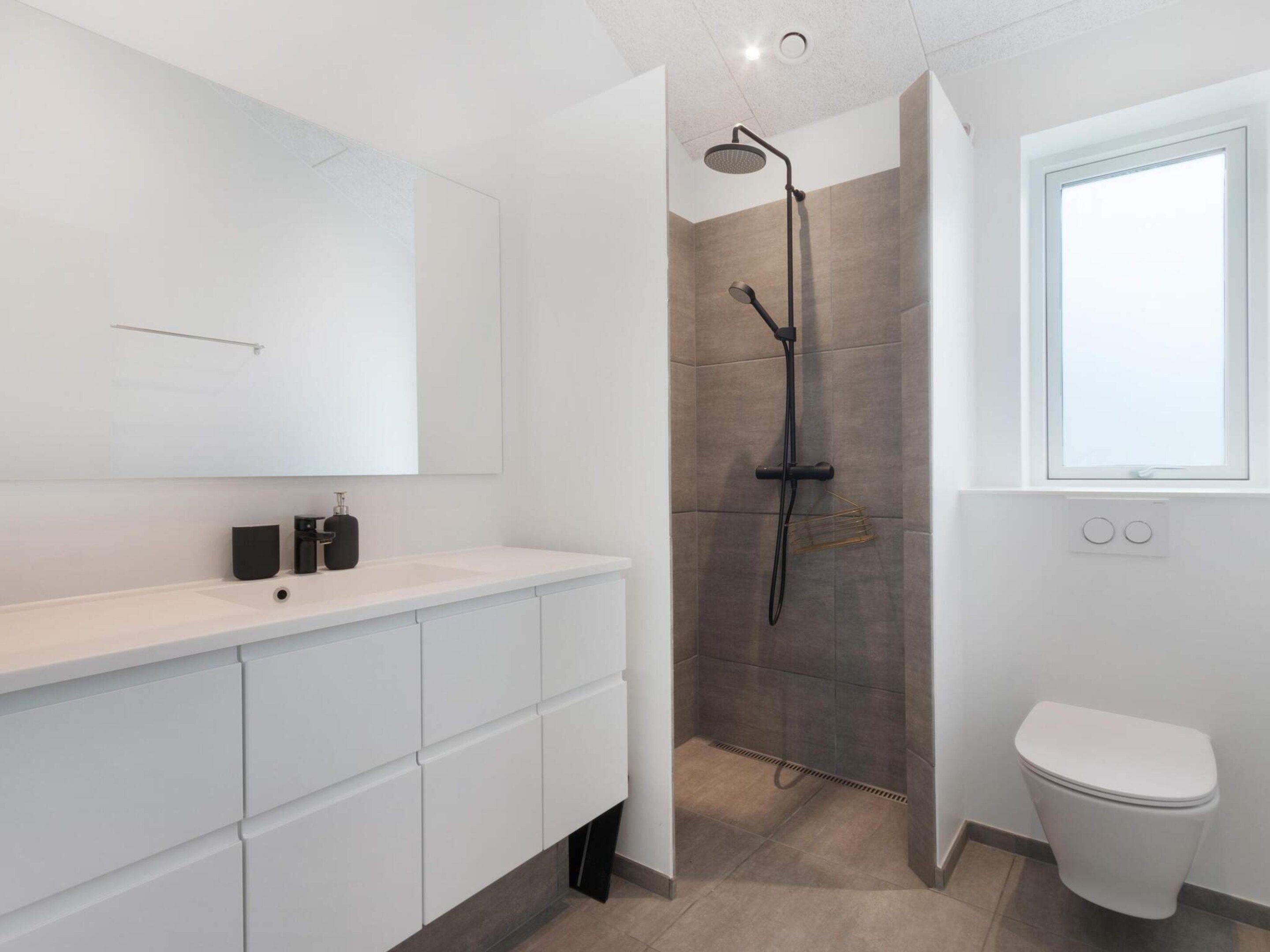 A modern bathroom with a shower, toilet, and a large mirror.