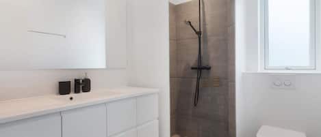 A modern bathroom with a shower, toilet, and a large mirror.