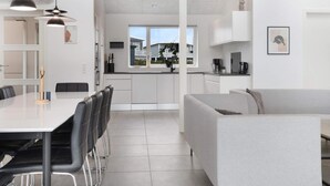 A modern kitchen with white cabinets, a dining area with a table and chairs, and a grey sofa. - 5 Star Holiday Home in Lokken (Lokken)