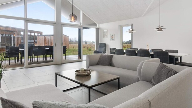 A spacious living area with a large sofa, a coffee table, and a dining area with chairs and a table. - 5 Star Holiday Home in Lokken (Lokken)