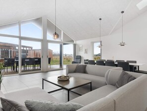 A spacious living area with a large sofa, a coffee table, and a dining area with chairs and a table. - 5 Star Holiday Home in Lokken (Lokken)