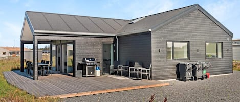 A modern house with a covered patio, a barbecue area, and a gravel driveway.