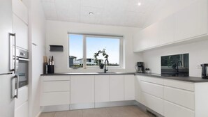 A modern kitchen with white cabinetry, a built-in oven, a sink, and a window offering a view of the outside. - 5 Star Holiday Home in Lokken (Lokken)