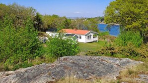 A white house with a red roof, surrounded by greenery and a large rock in the foreground. - 5 Star Holiday Home in Marstrand (Marstrand)