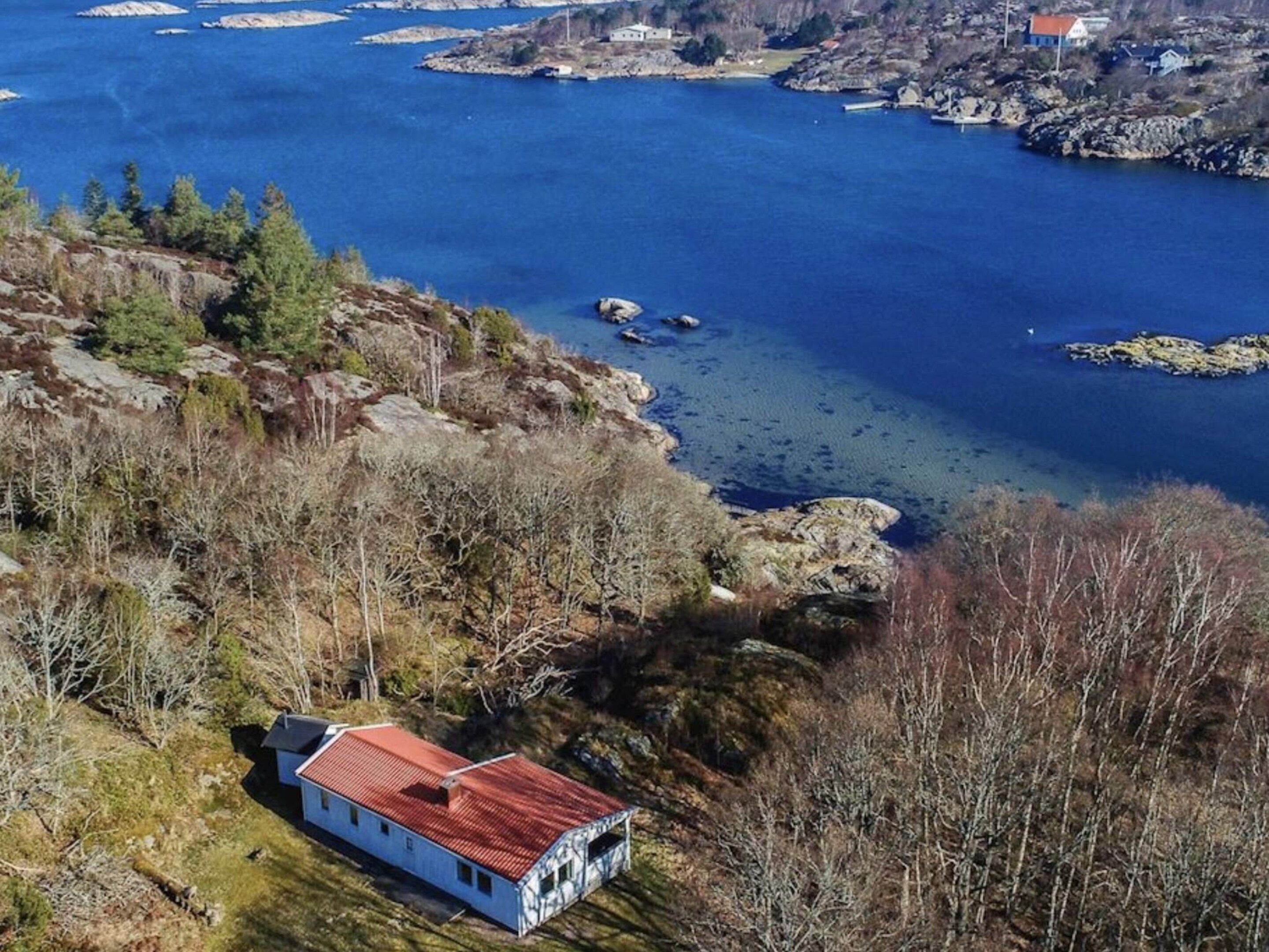 Uma propriedade costeira com uma casa numa rocha, água azul cristalina e vegetação rasteira.