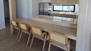 A modern kitchen with wooden cabinets, a stainless steel refrigerator, a built-in microwave, and a large island with a glass top.