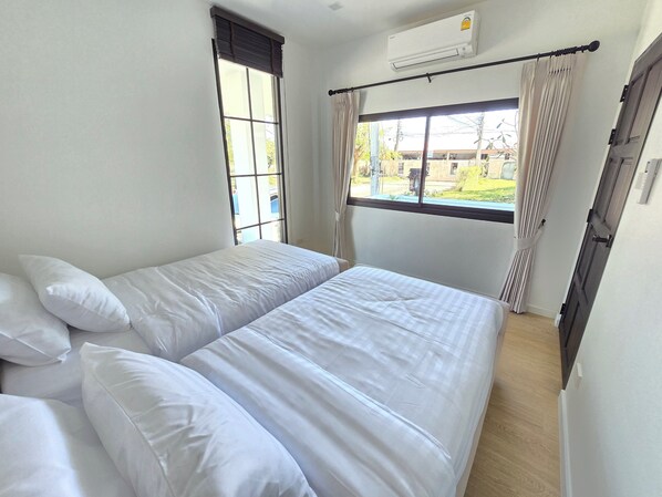 Una habitación con dos camas, una ventana con cortinas, un equipo de aire acondicionado y vistas al exterior.