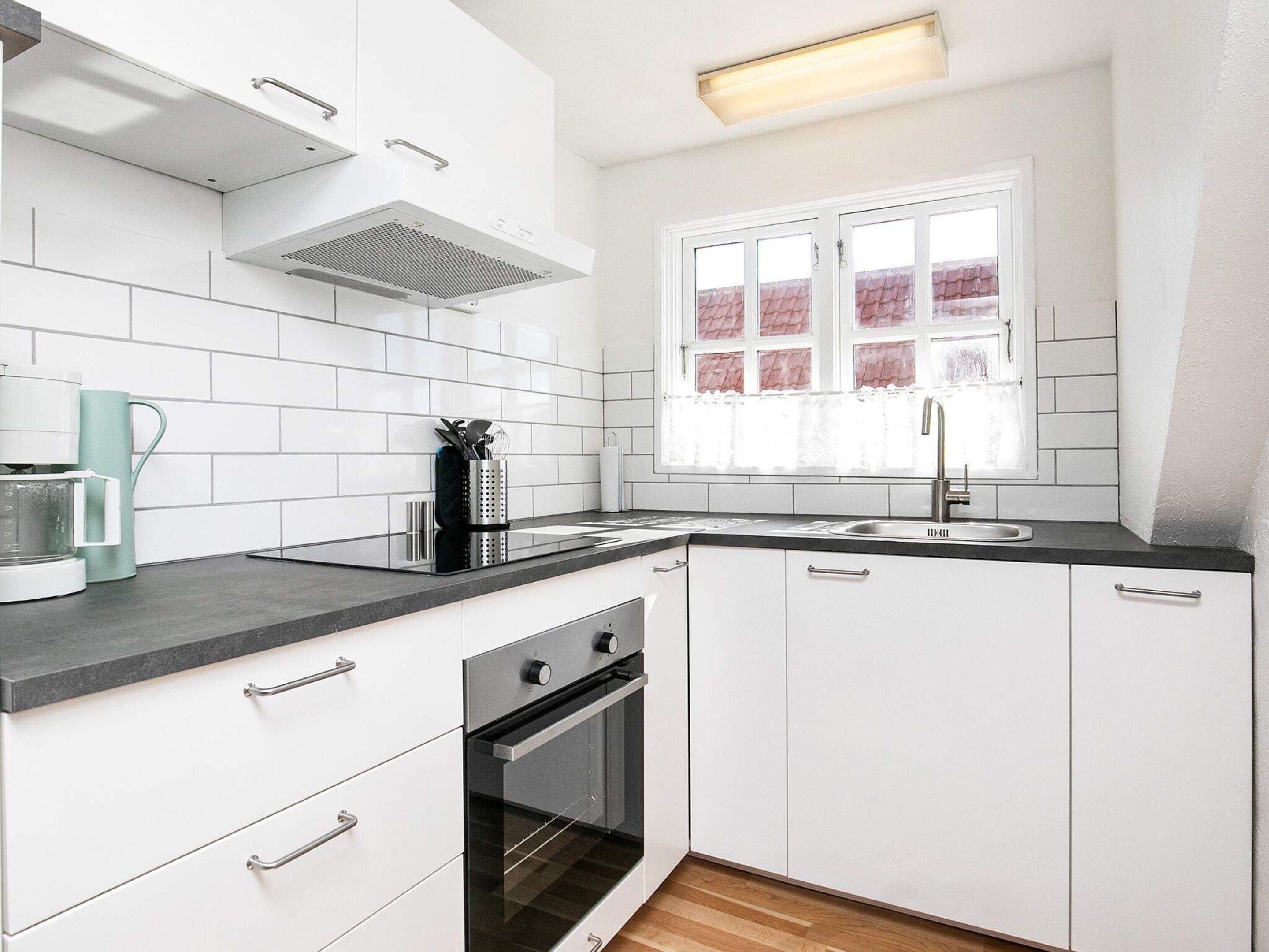 A modern kitchen with white cabinets, a built-in oven, a coffee maker, and a window with a view of a red-tiled roof.