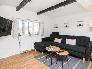Un salon moderne avec un canapé gris foncé, deux petites tables d’appoint rondes en bois, un tapis gris et un radiateur blanc.