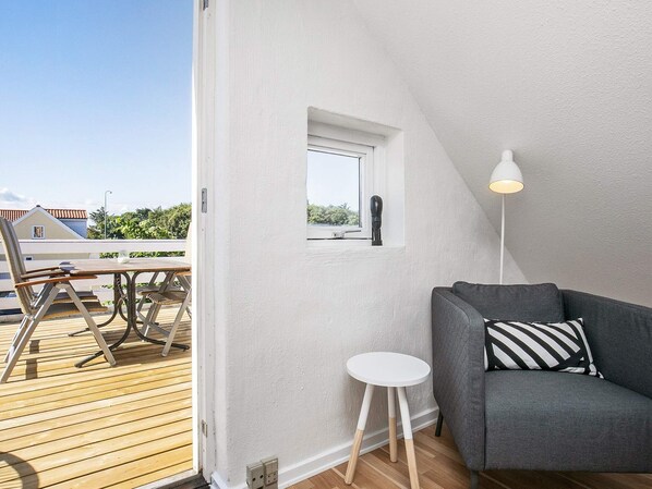 A room with a grey sofa, a small white table, and a lamp. There is a window with a view of greenery and a building outside. - 5 Star Holiday Home in Lokken (Lokken)