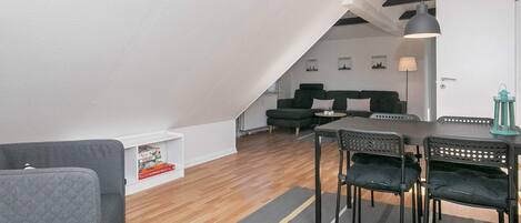 A modern loft-style living space with a dining area, a sofa set, and a staircase leading to an upper level.