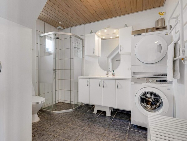 Un baño moderno con cabina de ducha de vidrio, un lavabo empotrado con espejo, un inodoro y una lavadora de carga frontal.