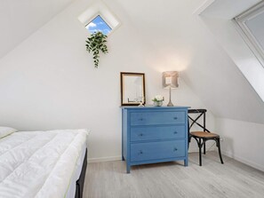 A bedroom with a bed, a blue dresser, a chair, a small table with a lamp, and a window with a plant. - 5 Star Holiday Home in Lokken (Lokken)