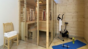 A sauna room with wooden walls and a glass door, a wooden chair with towels, a blue exercise mat, and a stationary bike. - Apartment in Kals Near Ski Slopes (Kals am Grossglockner)