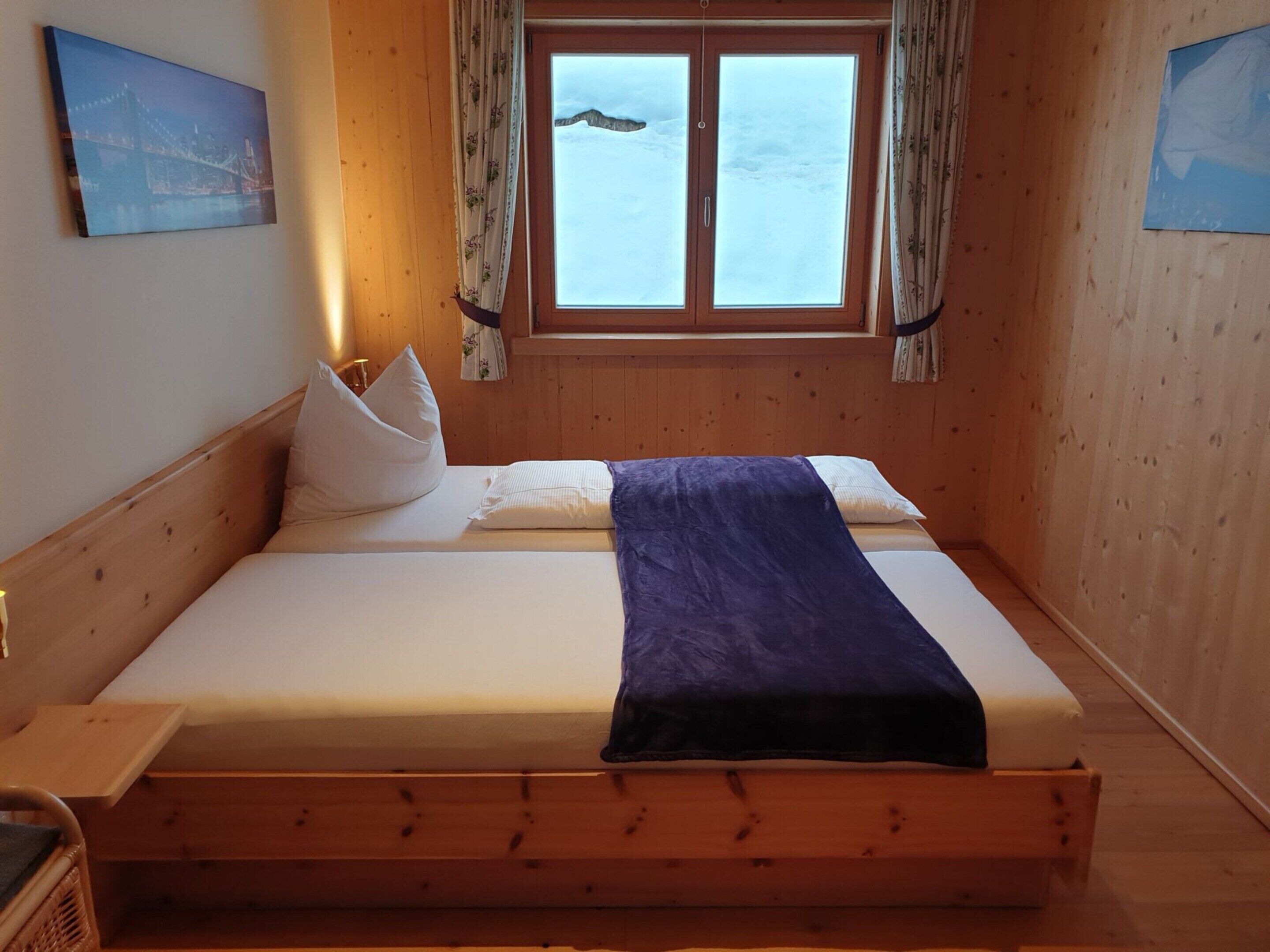 A wooden-paneled room with a bed, a window with curtains, and a painting on the wall.