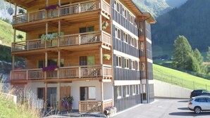 A multi-story wooden building with balconies, a car parked in front, and mountains in the background. - Apartment in Kals Near Ski Slopes (Kals am Grossglockner)