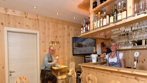 A wooden bar area with wooden chairs, a television mounted on the wall, and shelves with bottles and glasses. - Apartment in Kals Near Ski Slopes (Kals am Grossglockner)