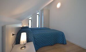 A bedroom with a bed, a bedside table with a lamp, and a window. - Detached villa with beautiful garden (Bibione)