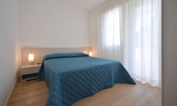 Un dormitorio con una cama, lámparas de noche y un ventanal con cortinas.