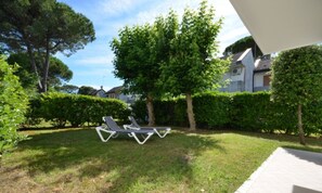 A garden area with two lounge chairs, a hedge, and a building in the background.