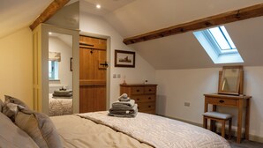A bedroom with a large bed, a wooden dresser, a small chair, a mirror, and a skylight. - Discover the charm of this wonderful barn, nestled in the Peak District. (Rushton Spencer)
