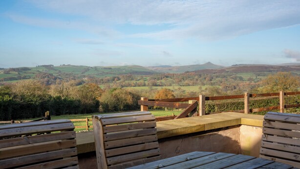 A wooden bench overlooking a scenic landscape with rolling hills and trees. - Discover the charm of this wonderful barn, nestled in the Peak District. (Rushton Spencer)