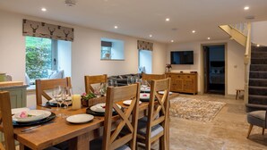 A dining area with a wooden table set for a meal, a sofa, and a staircase leading to another level. - Discover the charm of this wonderful barn, nestled in the Peak District. (Rushton Spencer)