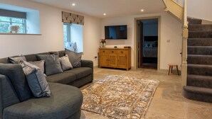 A living room with a grey sectional sofa, a wooden cabinet, a patterned rug, and a staircase. - Discover the charm of this wonderful barn, nestled in the Peak District. (Rushton Spencer)