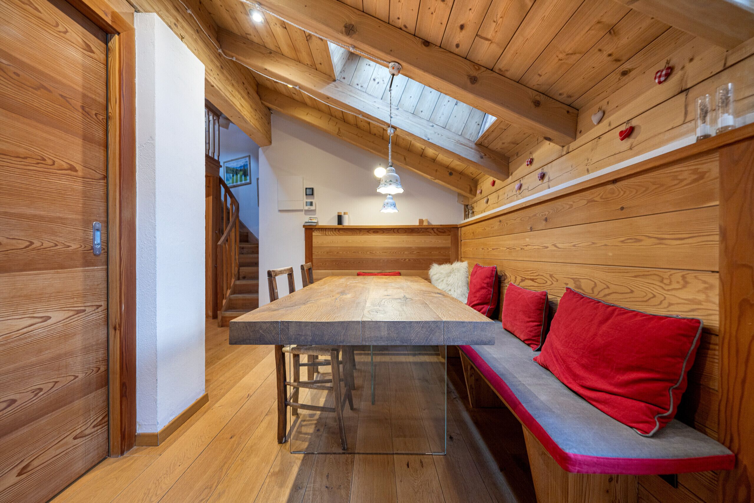 Un intérieur en bois avec un plafond haut, une table à manger et un banc doté de coussins rouges.