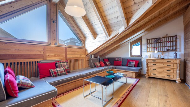 Un acogedor espacio tipo loft con techo de madera, un ventanal grande, un conjunto de sofás, una mesa de centro y un aparador.