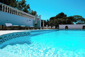 A swimming pool with a tiled edge, lounge chairs, and a white wall with a balustrade.