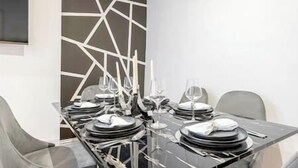 A modern dining table set with plates, glasses, and cutlery, surrounded by chairs. - Marylebone / Baker Street 2Bed (Greater London)