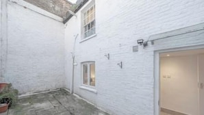 A white brick building with a small courtyard, a door with a light fixture, and a window. - Marylebone / Baker Street 2Bed (Greater London)