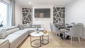 A modern living room with a sectional sofa, a dining table with chairs, and a decorative wall piece. - Marylebone / Baker Street 2Bed (Greater London)