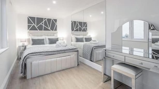 A modern bedroom with a large bed, a vanity with a mirror, and geometric wall art. - Marylebone / Baker Street 2Bed (Greater London)