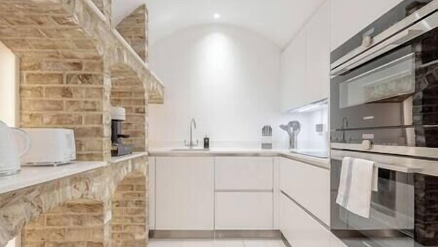 Eine moderne Küche mit einer Wandverkleidung aus Stein, einem eingebauten Backofen und weißen Schränken.