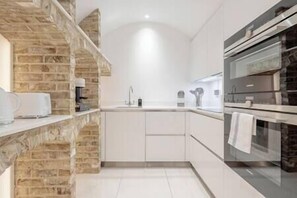 A modern kitchen with a stone accent wall, built-in oven, and white cabinetry. - The Marylebone Residence (Greater London)