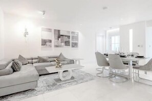 Un salon moderne avec un canapé d’angle gris, une table basse et un coin repas comprenant des chaises et une table.