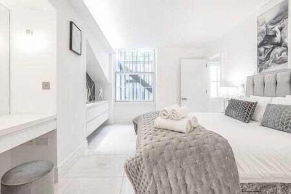 A modern bedroom with a large bed, a desk, and a window with a view of a staircase. - The Marylebone Residence (Greater London)