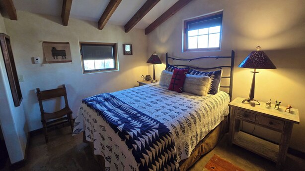 A bedroom with a bed, two bedside tables, a nightstand, a window, a chair, and a small table with decorative items. - Luxurious 2-bedroom cabin @ Canyon of the Ancients Guest Ranch in McElmo Canyon  (Cortez)