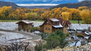 A rustic cabin with a metal roof, surrounded by a snowy landscape and autumn-colored trees. - Luxurious 2-bedroom cabin @ Canyon of the Ancients Guest Ranch in McElmo Canyon  (Cortez)