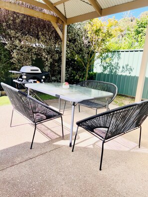 Relax outdoors with a covered seating area featuring a table and chairs, perfect for al fresco dining and barbecue.