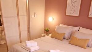 A neatly made bed with white linens and two folded towels, a bedside table with a lamp, and a framed abstract art piece on the wall. - Tranquil studio with AC in Rabat - Studio No.2  (Rabat)