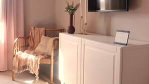 A living room with a television mounted on the wall, a wooden chair with a blanket, a white cabinet, and a woven rug. - Tranquil studio with AC in Rabat - Studio No.2  (Rabat)