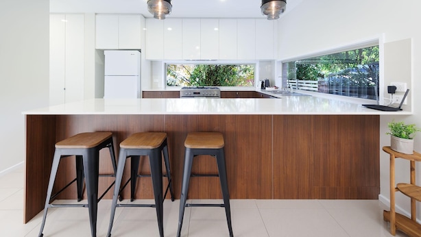 Une cuisine moderne dotée d’un grand îlot central, de tabourets en bois et de luminaires suspendus.