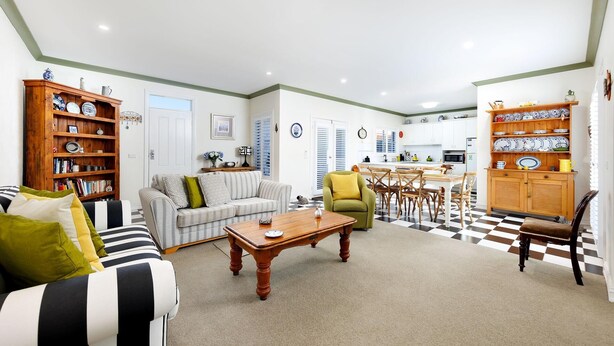 A living room with a sofa, armchairs, a coffee table, and a bookshelf. There is a dining area with a table and chairs.