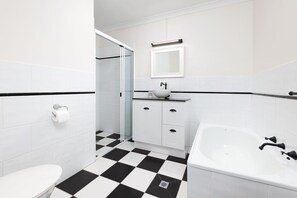 Ein modernes Badezimmer mit einem schwarz-weißen Schachbrettfußboden, einem weißen Waschbecken mit schwarzem Wasserhahn, einer weißen Badewanne und einer Dusche mit Glaswand.